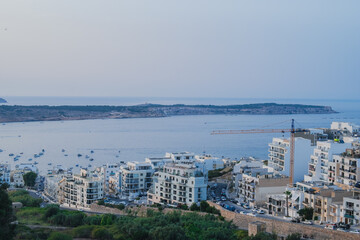 Obraz premium Mellieha bay skyline with many buildings and cranes in a beautiful sunset beach landscape