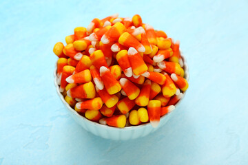 Bowl with tasty Halloween candy corns on blue background, closeup