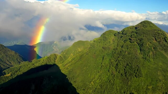 Animation of mountains with colorful rainbow in cloudy sky over field. Nature landscape after storm. Spring morning. St Patrick Day holiday symbol