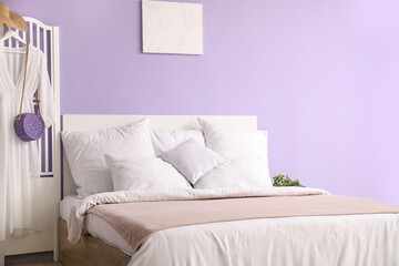 Interior of stylish bedroom with comfortable bed, white pillows and dress on folding screen