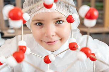 Portrait of a schoolgirl in a white coat demonstrating an atomic model of a molecule using a set of 3D atoms. Teenager studying chemical properties of elements in class