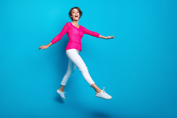 Full length photo of funky sweet lady dressed pink knitted shirt jumping high walking empty space isolated blue color background