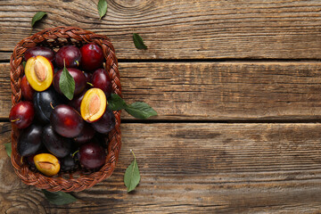 Wicker basket with fresh ripe plums and leaves on wooden background
