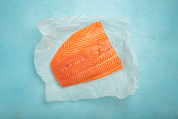 Fresh salmon fillet on wooden board against blue background, promoting healthy eating and gourmet...
