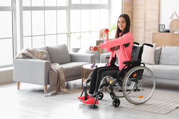 Sporty young woman in wheelchair with dumbbells training at home