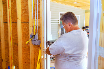 Using pneumatic nail gun, carpenter installs front door in new home