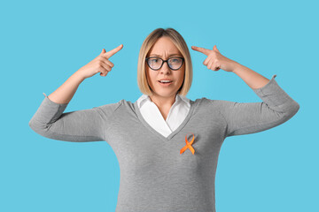 Beautiful mature shocked woman with ribbon pointing at head on blue background. Multiple Sclerosis...