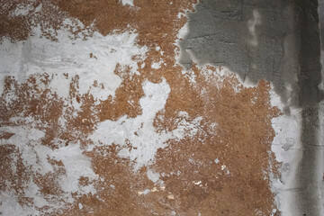 A close-up view of peeling plaster on an old wall revealing layers of texture and color variations in a dimly lit indoor setting