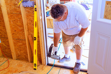 Installing front door of new house using pneumatic nail gun by carpenter