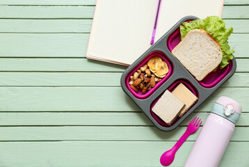 Lunch box with tasty food with bottle of water and school stationery on green wooden background