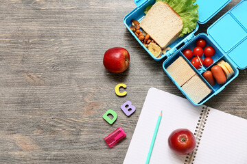 Lunch box with tasty food and school stationery on wooden background, top view