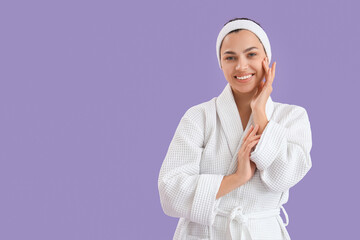 Beautiful young happy woman in bathrobe on purple background
