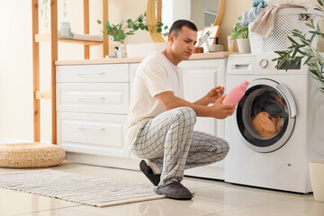Young man reading description of detergent near washing machine in laundry room