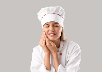 Young female chef suffering from tooth ache on grey background