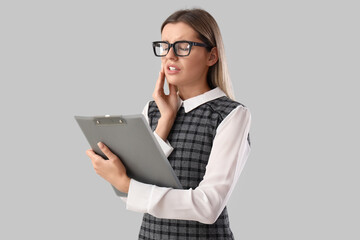 Young businesswoman with clipboard suffering from tooth ache on grey background