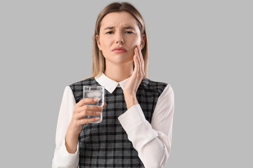 Young businesswoman with glass of cold water suffering from tooth ache on grey background