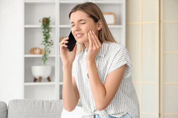 Young woman with tooth ache talking by phone at home