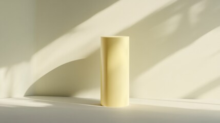 A tall yellow vase sits on a white surface, casting a shadow on the wall