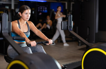 Active young woman engaged in arm workout on rowing equipment in exercise room