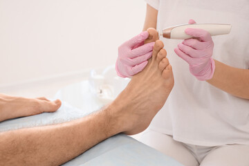 Beautician peeling feet of young man on couch in spa salon, closeup