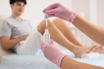 Young happy man getting professional pedicure with cuticle oil on couch in spa salon, closeup