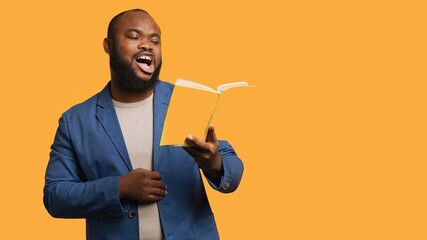 Man laughing while reading funny book, entertained by engrossing story. Joyful person having fun,...