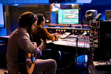 Young artist performer singing a new song on guitar in professional studio, sound engineer...