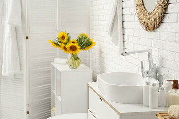 Sink and vase with sunflowers on shelving unit near white brick wall in restroom