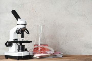 Modern microscope with chemical flask, protective glasses and notebooks on wooden table against...