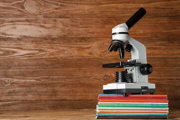 Modern microscope with copybooks on table against wooden background