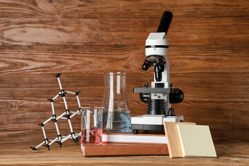 Modern microscope with chemical flasks, molecular model and books on table against wooden background