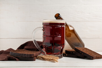 Mug of fresh kvass with slices of bread and wheat on white wooden background