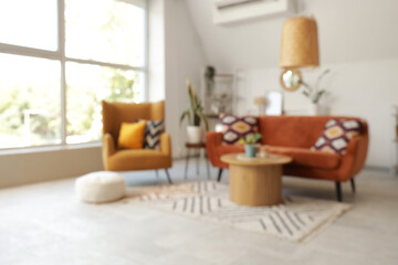 Blurred view of light living room with red sofa, armchair and table