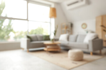 Blurred view of light living room with grey sofas, table and plants
