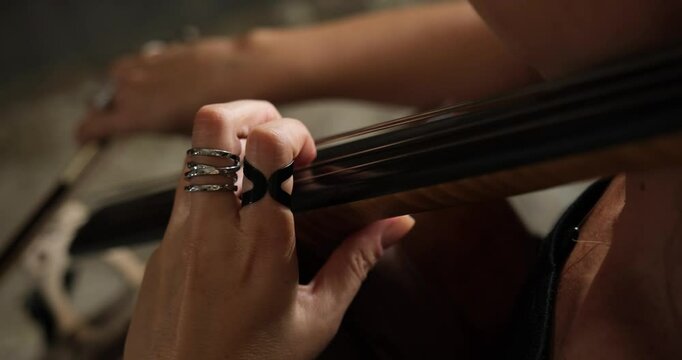 A middle-aged, white female musician wearing a black dress is playing the cello in an old building