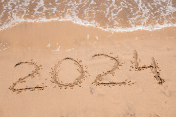 Looking ahead: The year '2024' emerges in the sand as the ocean waves softly approach, symbolizing the dawn of a new chapter.