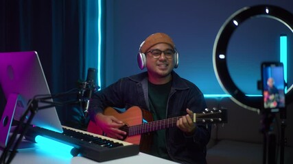 Happy Young asian musician enjoy playing guitar and singing a song in digital recording home studio dark room at night, a composer man mastering music audio for soundtrack live performance.
