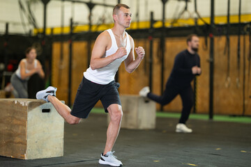 Sportive young guy practicing one leg squats with box in sports hall during crossfit workout