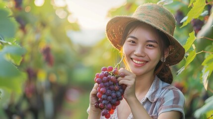 A smiling female farmer holding a bunch of grape in hand in plantation field in farm