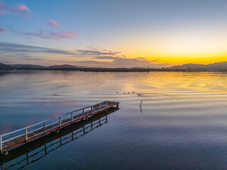 Obraz premium Sunrise along the waterfront with reflections on the bay water