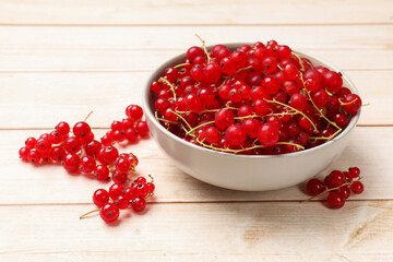 Fresh red currant berries in bowl on white wooden table