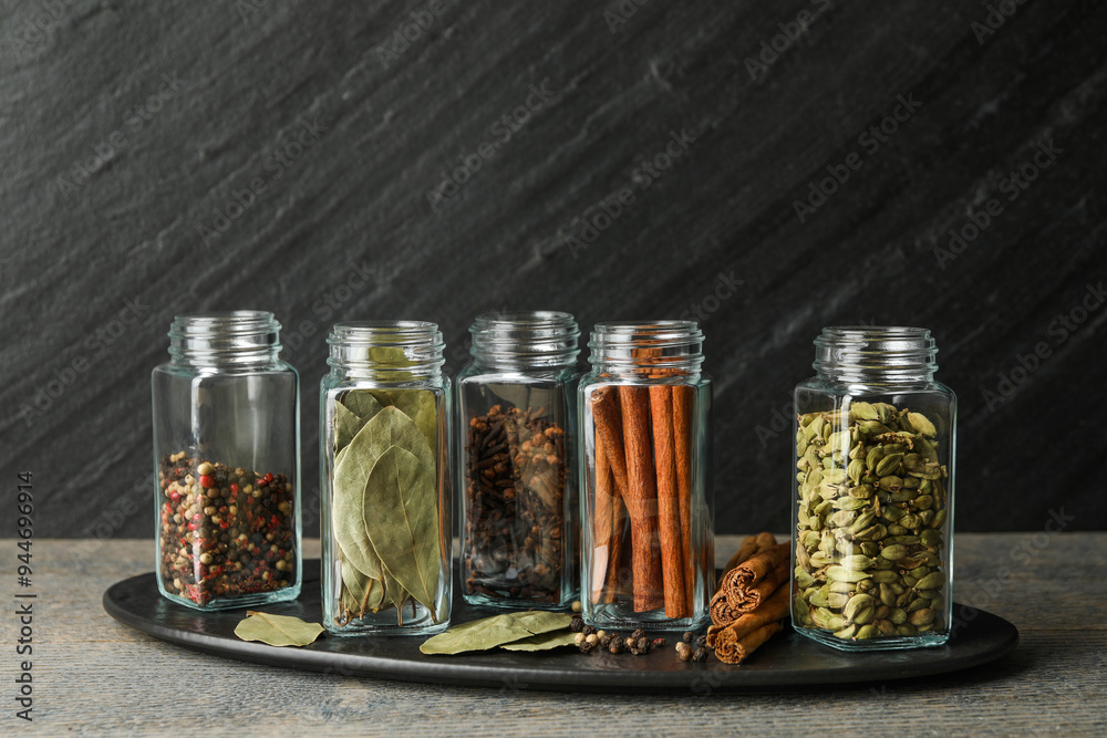 Sticker Different spices in glass jars on grey wooden table, closeup