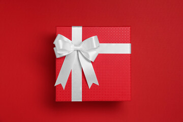 Gift box with white bow on red background, top view