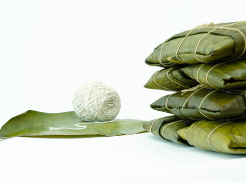 Hallacas envueltas en hojas de pl&aacute;tano, amarradas con pabilo, apiladas sobre mesa con fondo blanco