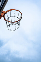 Naklejka premium Outdoor basketball hoop with chain net against cloudy sky.