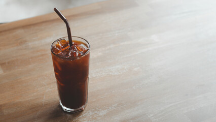 Ice americano coffee in a tall glass with ice cubes on a wood table. Cold summer drink with tubes on a table Black Russian Cocktail with Vodka and Coffee Liquor.