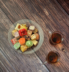 Two cups of hot tea and a plate with an assortment of various oriental sweets on a wooden table.