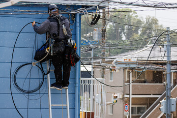 雨の日にアパートの電気工事をする作業員の後ろ姿