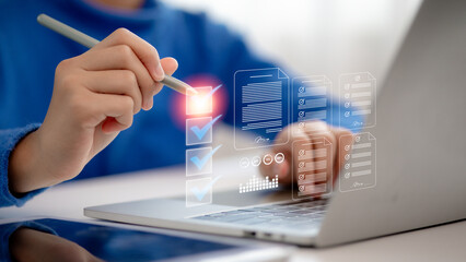 A businessman is using a laptop and tablet to complete online digital forms, fill out survey checklists, and assessment questionnaires as part of a business performance checklist and tracking process