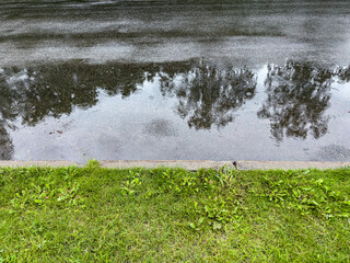 wet asphalt road with puddle, street concrete curb and roadside grass. cityscape after rain.